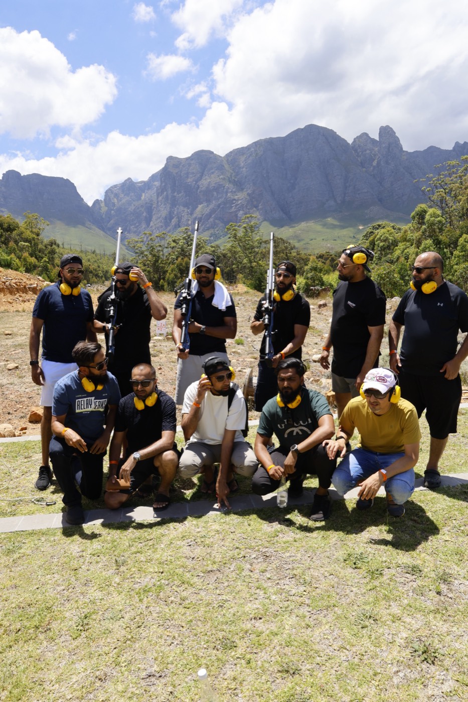 A group of shooters on the Rowe range, ear defenders around their necks, with the Helderberg mountains behind them.